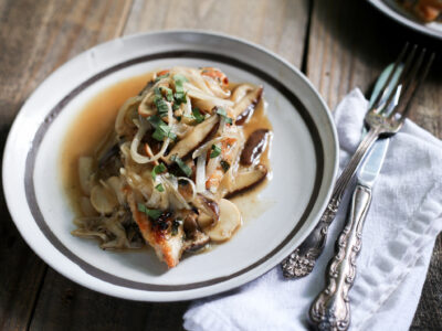 chicken breast with wild mushrooms and tarragon sauce on brown plate with silverware and napkin