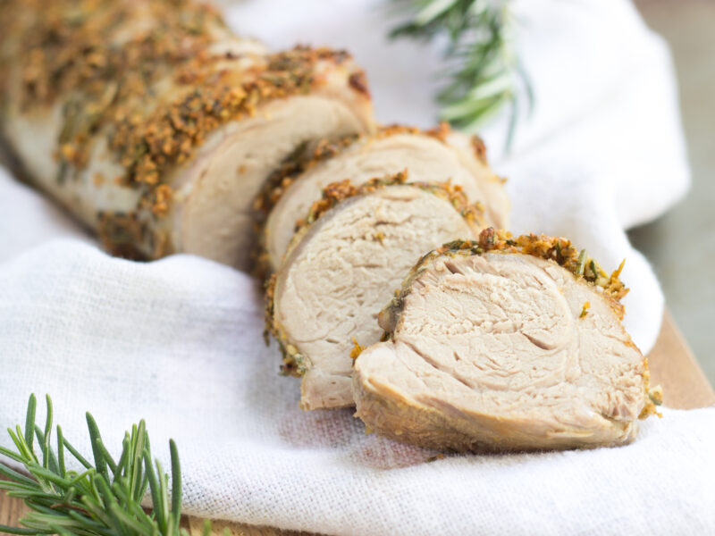 herb crusted pork loin on white towel with rosemary