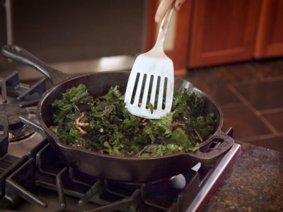 Wide shot of cooking kale with bacon in a cast iron skillet