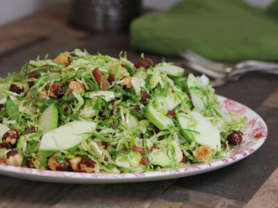 Shaved Brussels Slaw with Hazelnuts, Apples, and Mint on a decorative plate sitting on a wood table