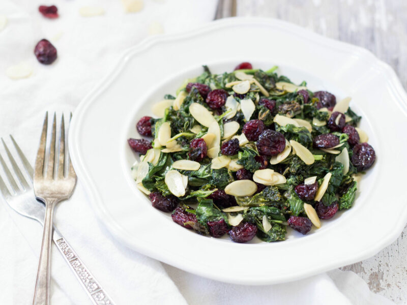 Wide shot of wilted spinach salad with almonds and cranberries in a white bowl.
