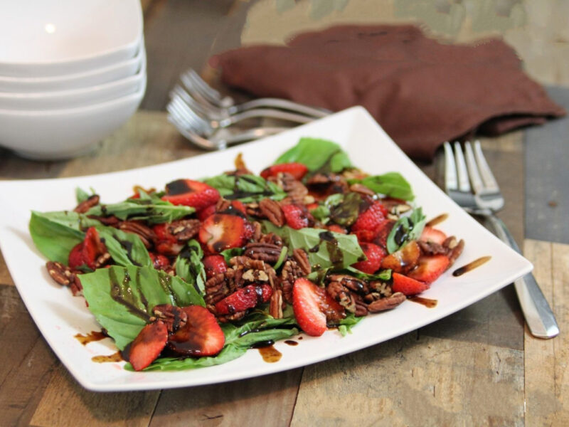 Wide shot of stawberry, basil, pecan salad on a rectangular plate on a wood table.