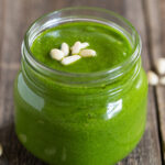 Clear glass jar of Lemon-Basil Pesto with sprinkles of pine nuts on a wood table - wide shot.