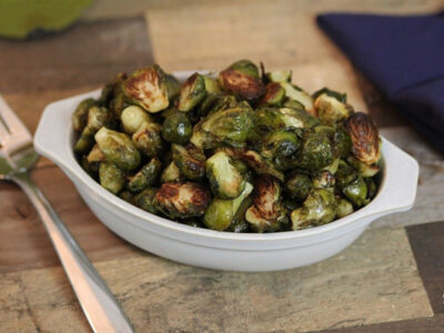 Image of roasted Brussels sprouts in white oval dish on wood table