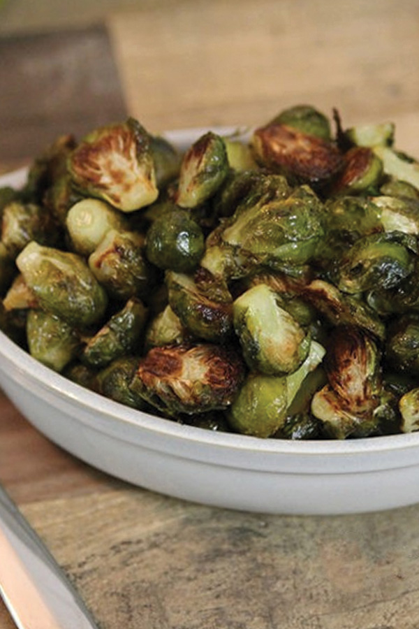 Close up of roasted Brussels sproutps in a white dish on a wood table/