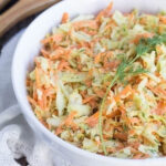 Wide image of coleslaw in a white bowl and a white napkin in the background.