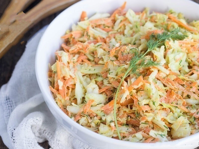 Wide image of coleslaw in a white bowl and a white napkin in the background.