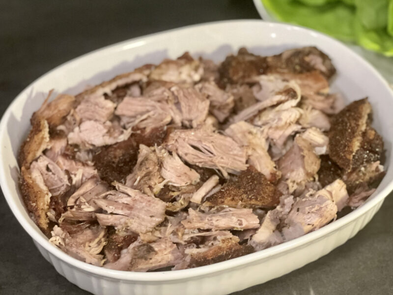 Wide shot of pulled pork in a white casserole dish on dark gray background.