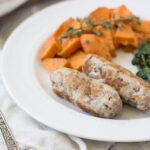Horizontal image of two homemade pork links with sweet potato and greens on a white plate.