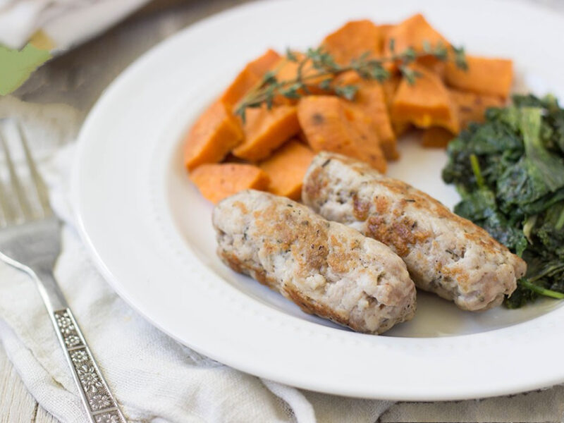 Horizontal image of two homemade pork links with sweet potato and greens on a white plate.