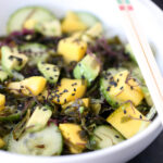 Wide image of Avocado Mango Seaweed Salad in a white bowl with chopsticks balancing on the side of the bowl