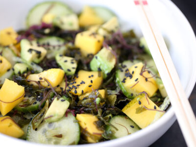 Wide image of Avocado Mango Seaweed Salad in a white bowl with chopsticks balancing on the side of the bowl