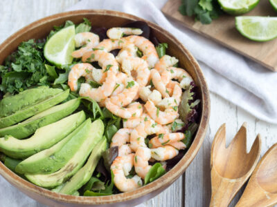 Wide image of Shrimp and Avocado Salad in a wooden bowl with wooden utensils near by