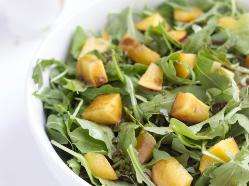 Wide image of apricot and Arugula salad with balsamic vinaigrette in a white bowl