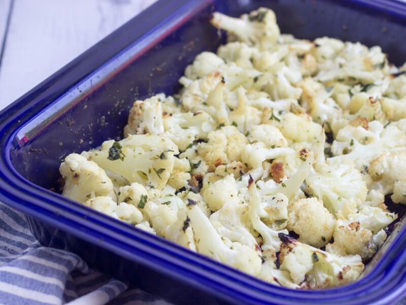 Wide shot of roasted cauliflower in a blue ceramic casserole dish.