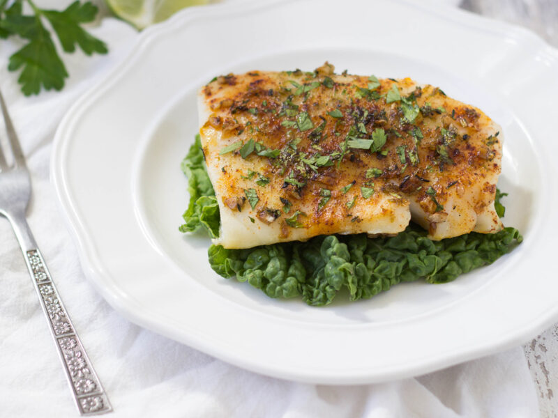 Horizontal Image of Garlic-Margarita Whitefish sprinkled with paprika and parsley on a white plate.