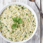 Wide image of Lemon Parsley Cauliflower "Rice" in a white bowl with a white and gray distressed wood background.