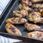 Wide image of Asian-Inspired Chicken wings on a black sheet pan with a blue and white stripped napkin.