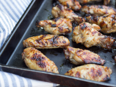Wide image of Asian-Inspired Chicken wings on a black sheet pan with a blue and white stripped napkin.
