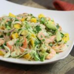 Wide image of Shrimp, Mango, Avocado, and Fennel Salad in a square bowl on a wood table.