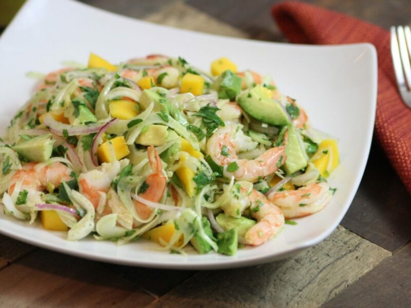 Wide image of Shrimp, Mango, Avocado, and Fennel Salad in a square bowl on a wood table.