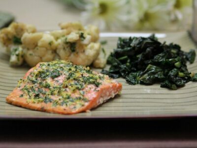 Wide image of Lemon-Tarragon Salmon on a neutral square plate with a side of greens and cauliflower.