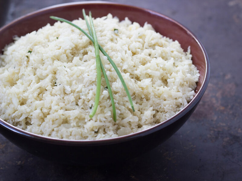 Wide shot of Ginger-Garlic Cauliflower Rice in a Bowl topped with a few sprigs of chives.