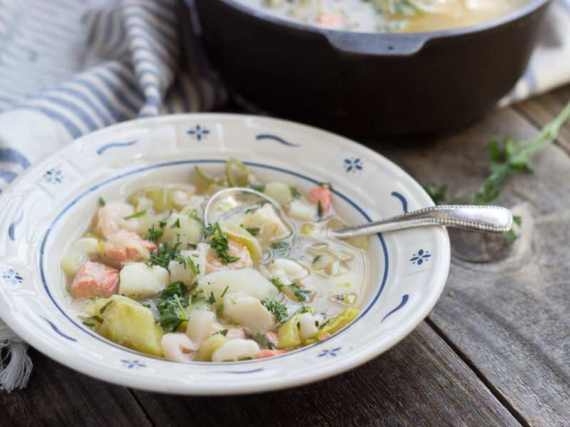 Seafood Leek Soup in a bowl with an antique soup spoon with full pot of soup in the background.