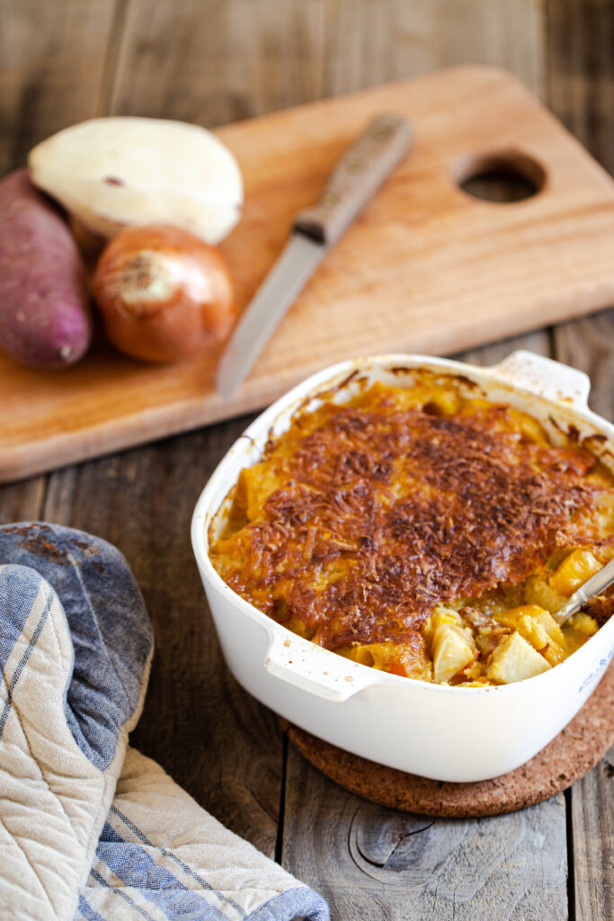 root vegetables in white casserole dish with onions on cutting board