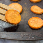 Baked Spiced Sweet Potato (circle cut) on a seasoned baking sheet with potato lifted on wooden spatula.
