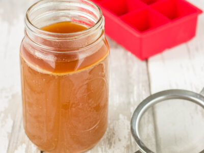 Image of Long-Simmered Chicken Bone Broth in wide-mouth mason jar on a light wood background.