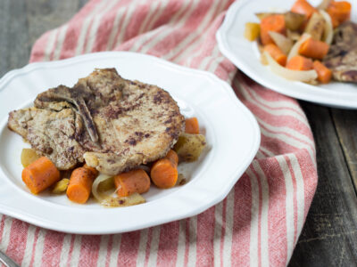 Braised Pork Chops served over braised vegetables like carrots and onions in a white bowl with a second serving visible in the background.