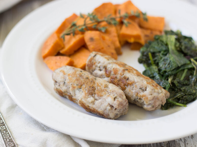 Homemade pork sausage with dried herbs and spices cook and plated wtih sauteed greens and sweet potatoes