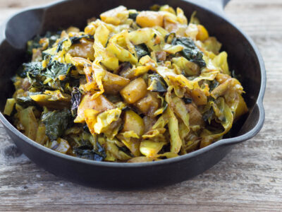 Curry Kale and Cabbage in cast iron pan on a wood background.