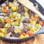 Horizontal image of pressure cooker lamb stew with acorn squash, carrots, and onions presented in a cast iron pan.
