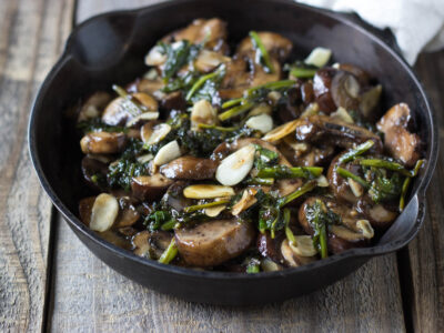Stir-Fried Turnips with Mushrooms, Almonds, Ginger, and Garlic pictured in a Cast Iron Pan on a wood table.