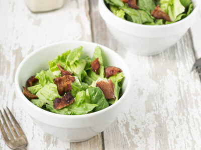 Ceasar Salad with Bacon in a white bowl on a distressed white wood table.