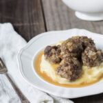 Grain-free Swedish Meatballs served over cauliflower puree and gravy in a white bowl.