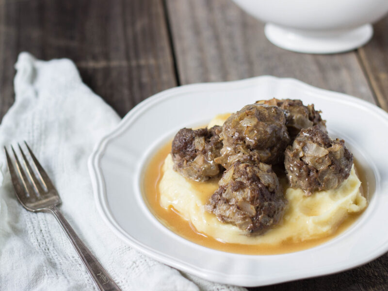 Grain-free Swedish Meatballs served over cauliflower puree and gravy in a white bowl.