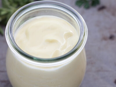 Small clear jar filled with homemade mayonnaise on a neutral background.
