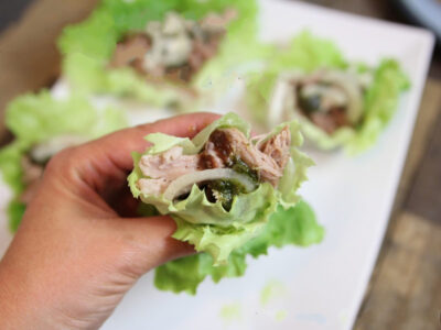 Close up of a single Pulled-Pork-Lettuce-Wrap with more on a white plate blurred in the background