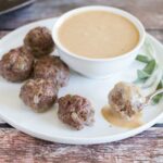 Asian meatballs on white plate with dipping sauce in white bowl.