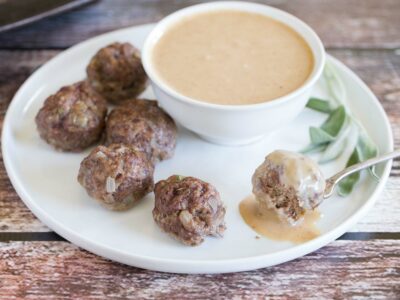 Asian meatballs on white plate with dipping sauce in white bowl.