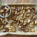 Roasted Brazil Nuts on a parchment -ined sheet pan with some in a small white bowl.
