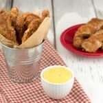 Grain-free chicken fingers in a small galvanized bucket over red chicken background.