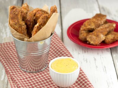 Grain-free chicken fingers in a small galvanized bucket over red chicken background.