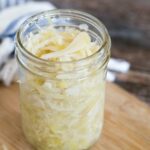 Sauerkraut in a small glass jar on a light wood counter.