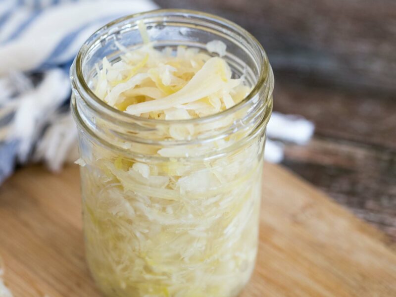Sauerkraut in a small glass jar on a light wood counter.