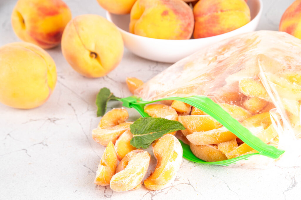 An image of frozen peach slices in a plastic bag, alongside fresh peaches.