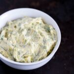 Creamy room temperature herbed compound butter in a white bowl on a dark background.